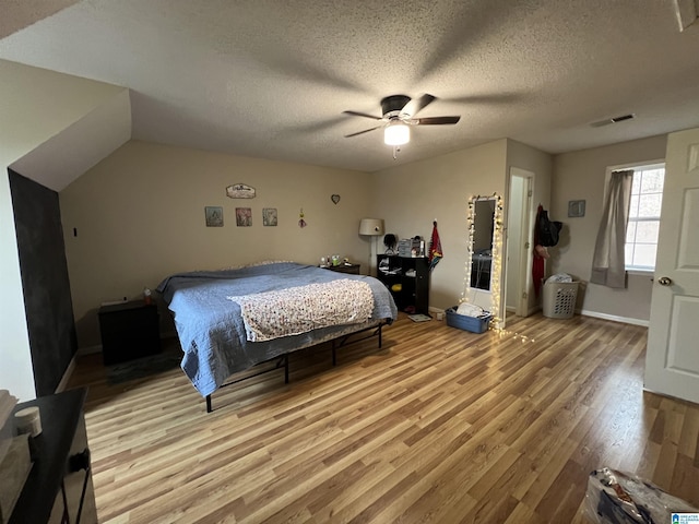 bedroom with a textured ceiling, ceiling fan, visible vents, baseboards, and light wood finished floors