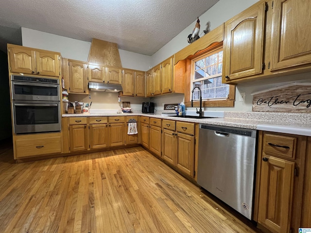 kitchen with light wood finished floors, stainless steel appliances, light countertops, under cabinet range hood, and a sink