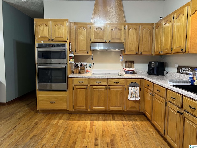 kitchen featuring black electric stovetop, light countertops, light wood-type flooring, under cabinet range hood, and double oven