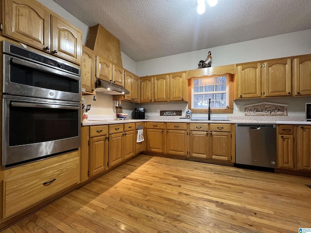 kitchen featuring light countertops, appliances with stainless steel finishes, a sink, light wood-type flooring, and under cabinet range hood