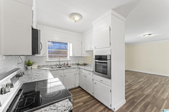 kitchen with appliances with stainless steel finishes, dark wood-style flooring, a sink, white cabinetry, and backsplash