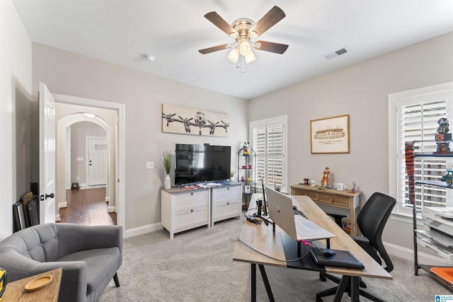 office area with arched walkways, ceiling fan, a wealth of natural light, and visible vents