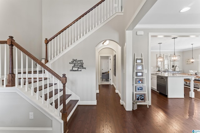 stairs with arched walkways, a towering ceiling, baseboards, wood-type flooring, and crown molding