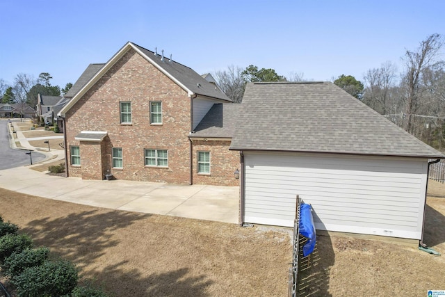 view of front of house with a shingled roof, a patio area, brick siding, and driveway