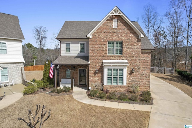 traditional home with roof with shingles, fence, and brick siding