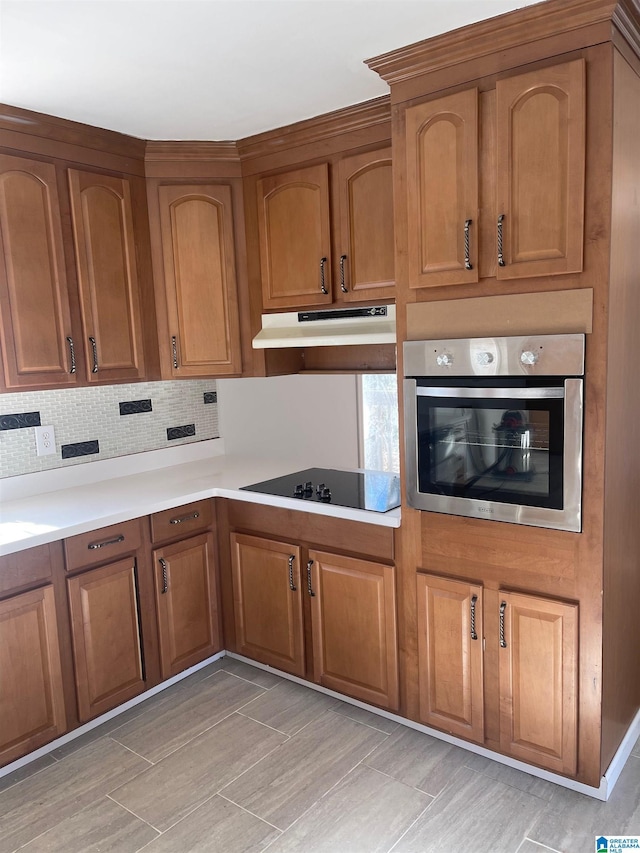 kitchen with light countertops, brown cabinetry, stainless steel oven, under cabinet range hood, and black electric cooktop