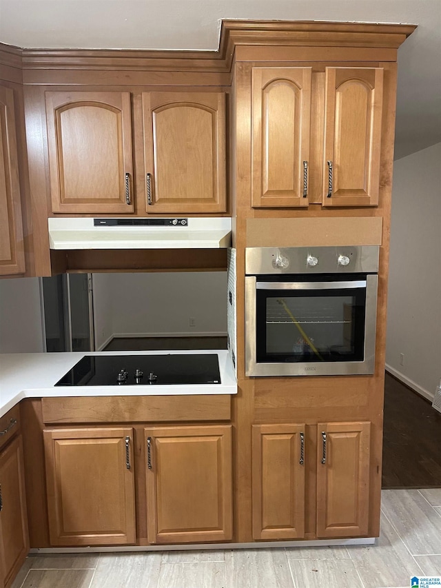 kitchen with black electric cooktop, oven, under cabinet range hood, light wood-style floors, and light countertops