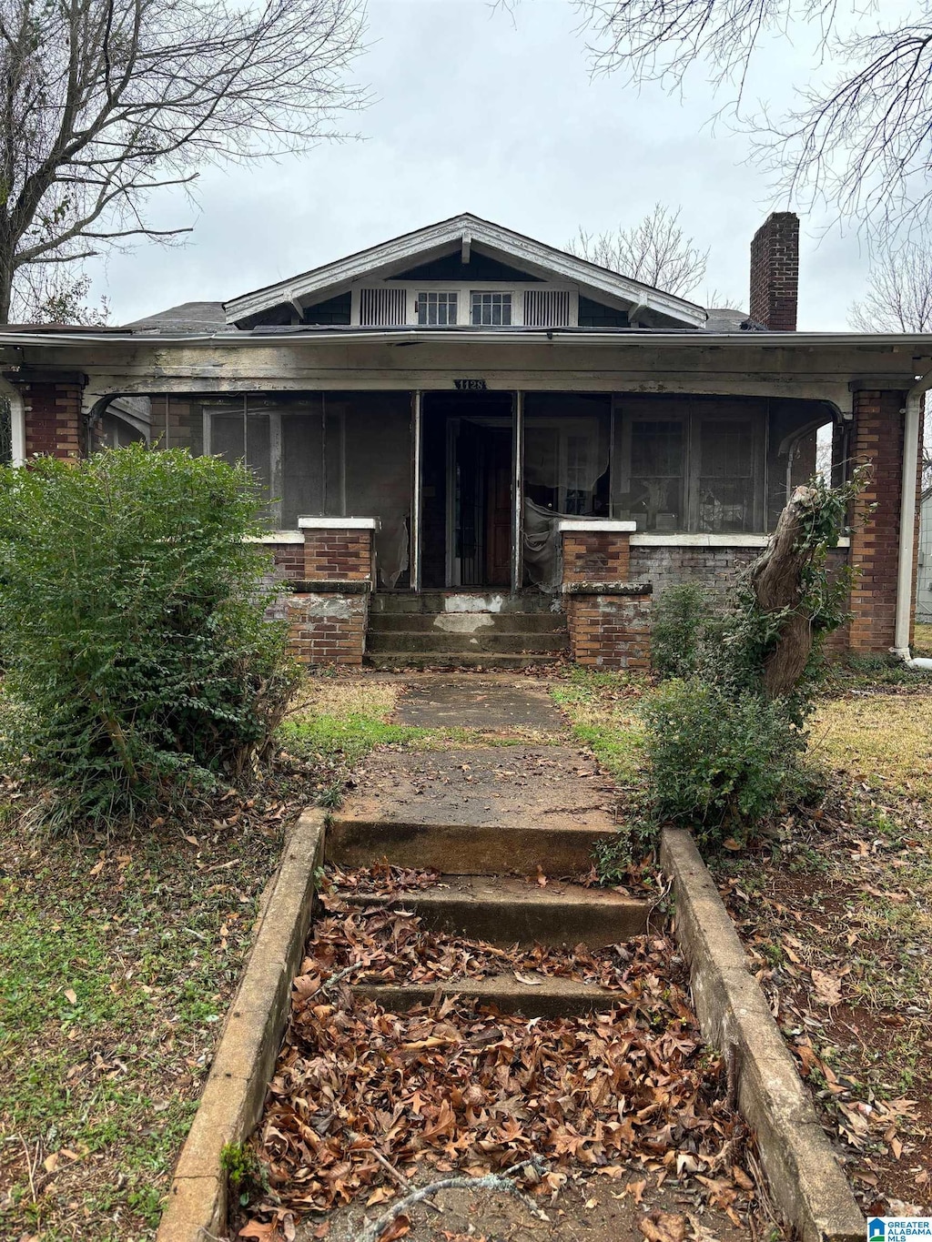 bungalow-style home with a sunroom, a chimney, a porch, and brick siding