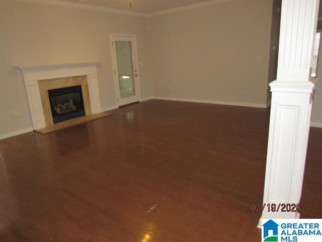 unfurnished living room with baseboards, ornamental molding, wood finished floors, and a glass covered fireplace