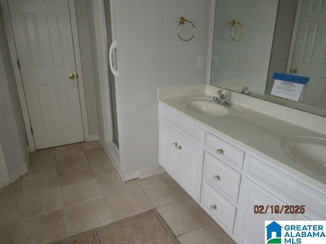 full bath featuring double vanity, a stall shower, a sink, and tile patterned floors