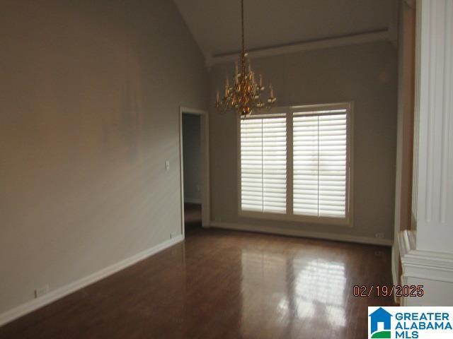 empty room featuring wood finished floors, vaulted ceiling, baseboards, and an inviting chandelier