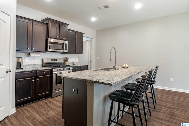 kitchen featuring stainless steel appliances, visible vents, dark wood-type flooring, a sink, and a kitchen breakfast bar