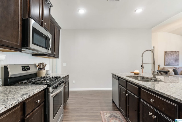 kitchen featuring appliances with stainless steel finishes, a sink, dark brown cabinets, light stone countertops, and baseboards