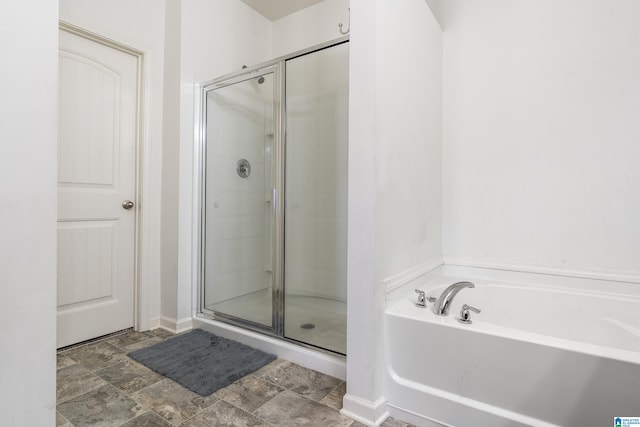 bathroom with a stall shower, stone finish flooring, baseboards, and a bath