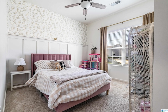 carpeted bedroom featuring a wainscoted wall, a ceiling fan, visible vents, and wallpapered walls