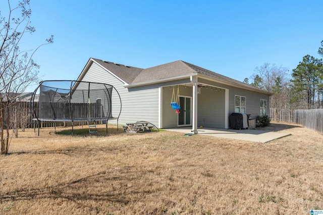 rear view of property with a trampoline, a yard, a shingled roof, a patio area, and a fenced backyard