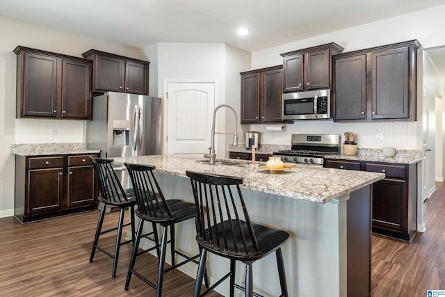 kitchen with stainless steel appliances, a sink, dark brown cabinets, and dark wood-style floors