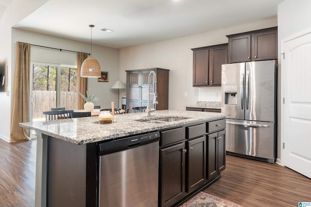 kitchen featuring light stone counters, dark wood finished floors, stainless steel appliances, a kitchen island with sink, and a sink