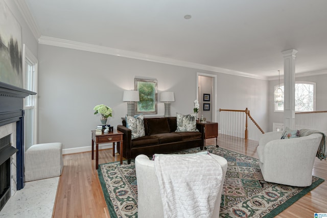 living room featuring ornate columns, a fireplace with flush hearth, ornamental molding, light wood-type flooring, and baseboards