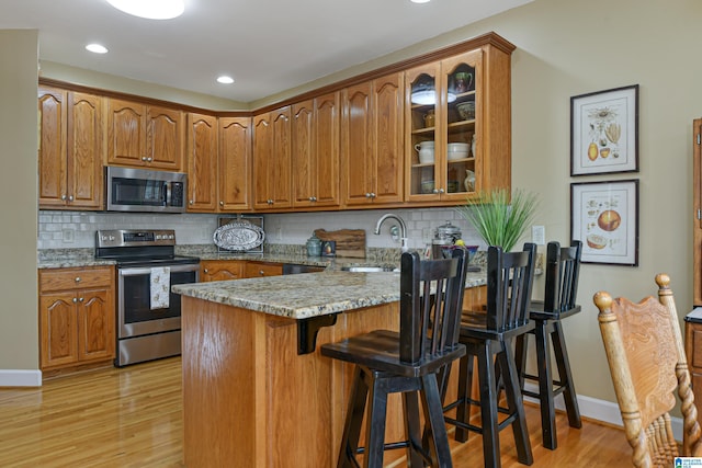 kitchen with brown cabinets, appliances with stainless steel finishes, a sink, light stone countertops, and a peninsula