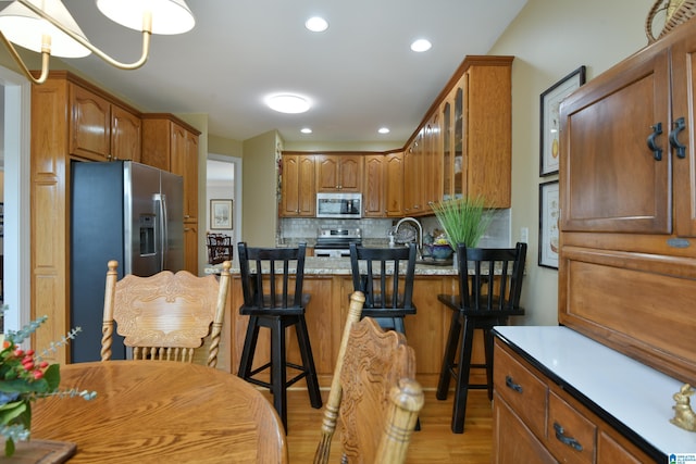 kitchen with brown cabinetry, decorative backsplash, a breakfast bar area, glass insert cabinets, and stainless steel appliances