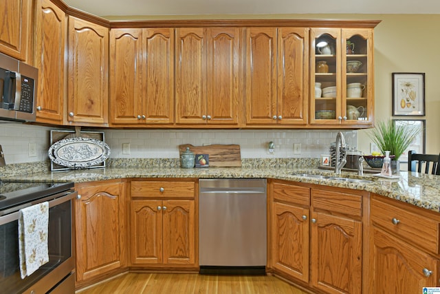 kitchen with light stone counters, brown cabinets, stainless steel appliances, glass insert cabinets, and a sink