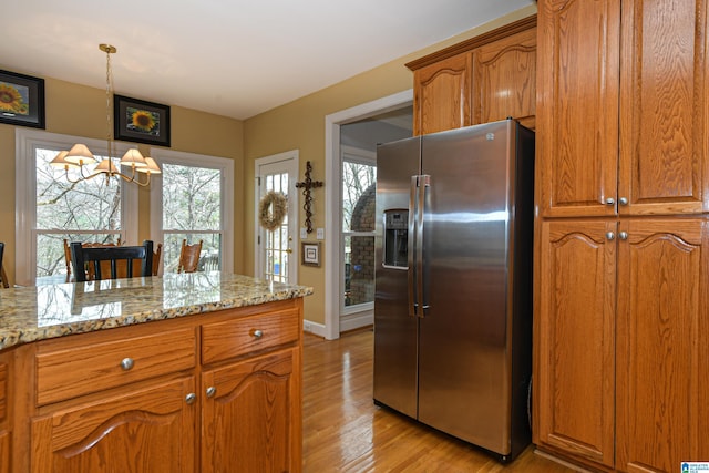 kitchen with brown cabinetry, light stone counters, pendant lighting, light wood-style floors, and stainless steel refrigerator with ice dispenser