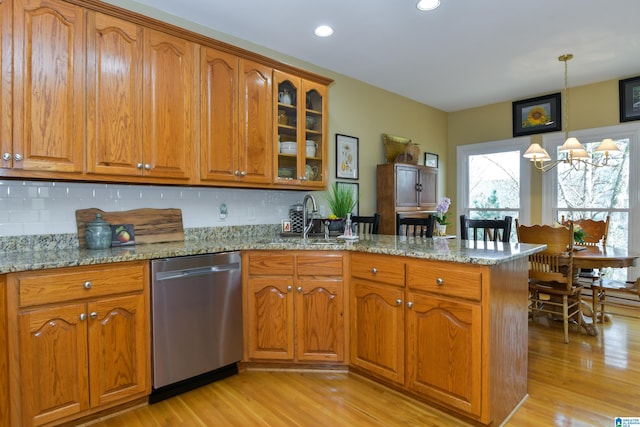 kitchen featuring stainless steel dishwasher, brown cabinetry, glass insert cabinets, light stone countertops, and a peninsula