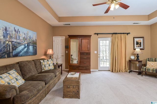 living room with a tray ceiling, light colored carpet, ceiling fan, and visible vents