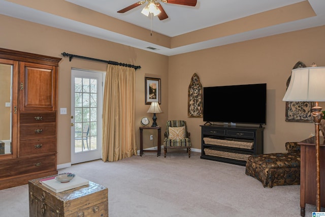 carpeted living room with a tray ceiling, a ceiling fan, visible vents, and baseboards