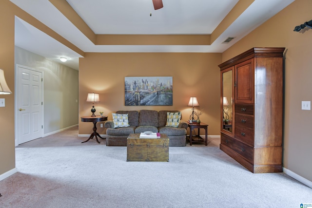 living area with baseboards, visible vents, a ceiling fan, light colored carpet, and a tray ceiling