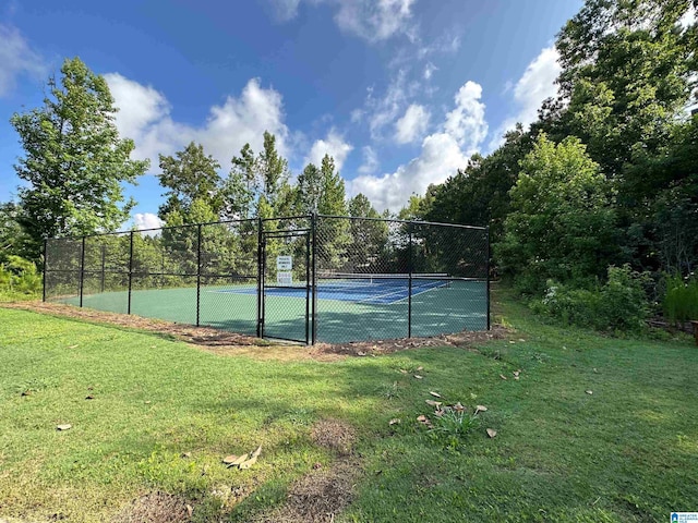 view of tennis court with a lawn and fence