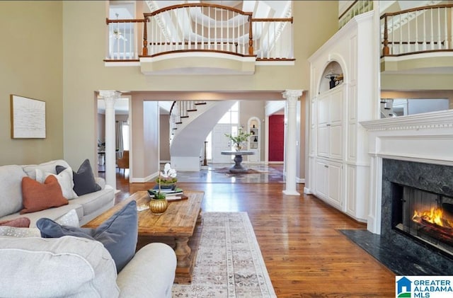 living area featuring a towering ceiling, decorative columns, a fireplace, and wood finished floors