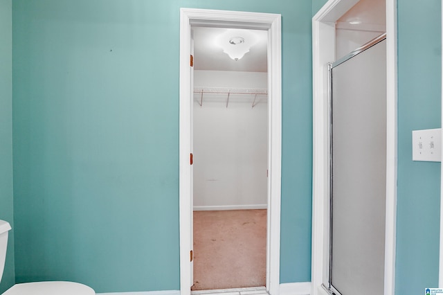 full bath featuring a stall shower, a walk in closet, and toilet