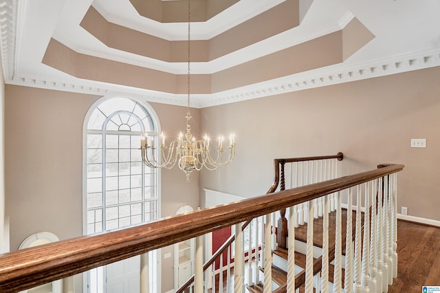 corridor with baseboards, a raised ceiling, dark wood finished floors, crown molding, and an upstairs landing