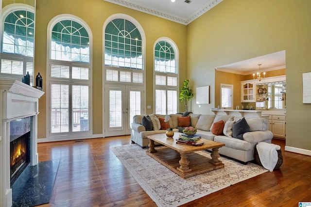 living room featuring a fireplace, a towering ceiling, baseboards, dark wood-style floors, and crown molding