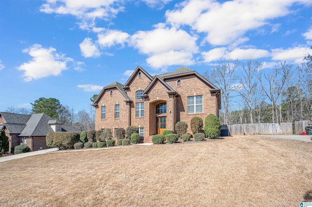 traditional-style home featuring brick siding, a front lawn, and fence