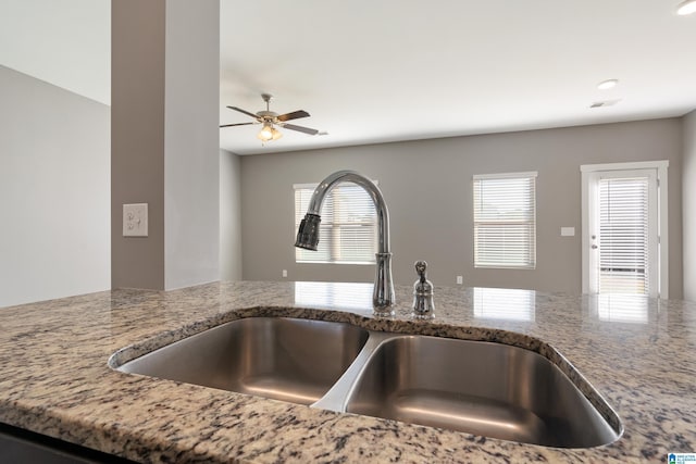 room details with ceiling fan, a sink, and light stone countertops