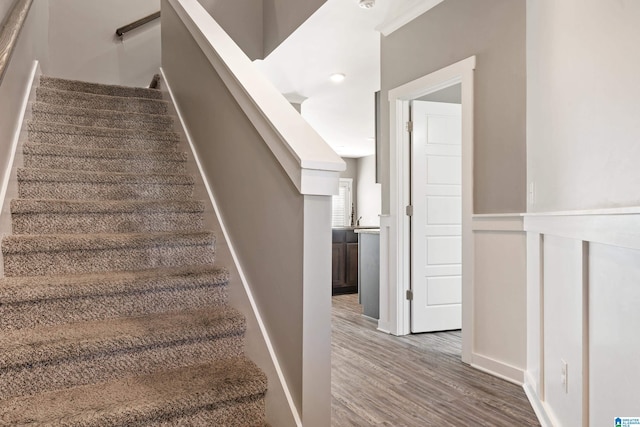 stairs featuring wainscoting and wood finished floors