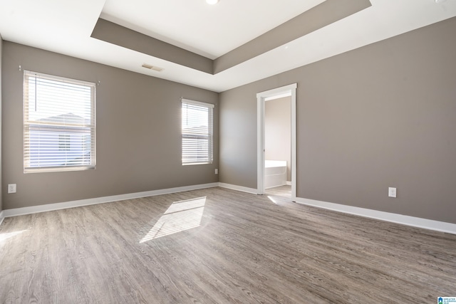 unfurnished room featuring a raised ceiling, visible vents, baseboards, and wood finished floors