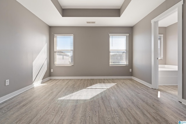 empty room with baseboards, a tray ceiling, visible vents, and a healthy amount of sunlight