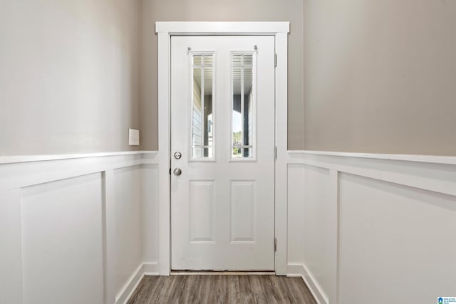 doorway featuring a decorative wall, wood finished floors, and wainscoting