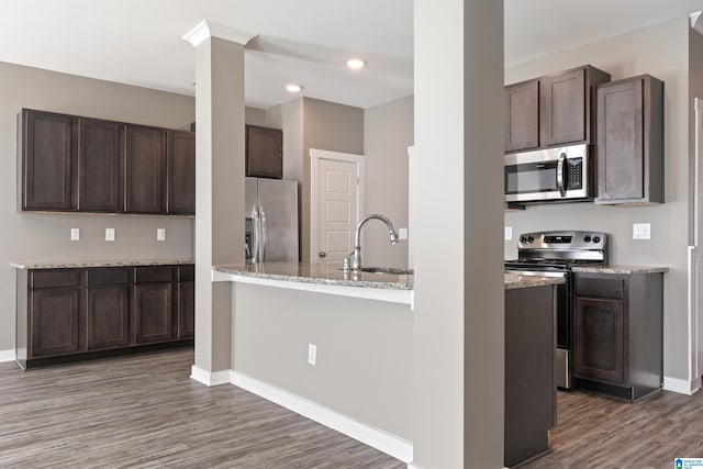 kitchen featuring dark brown cabinetry, baseboards, appliances with stainless steel finishes, wood finished floors, and a sink