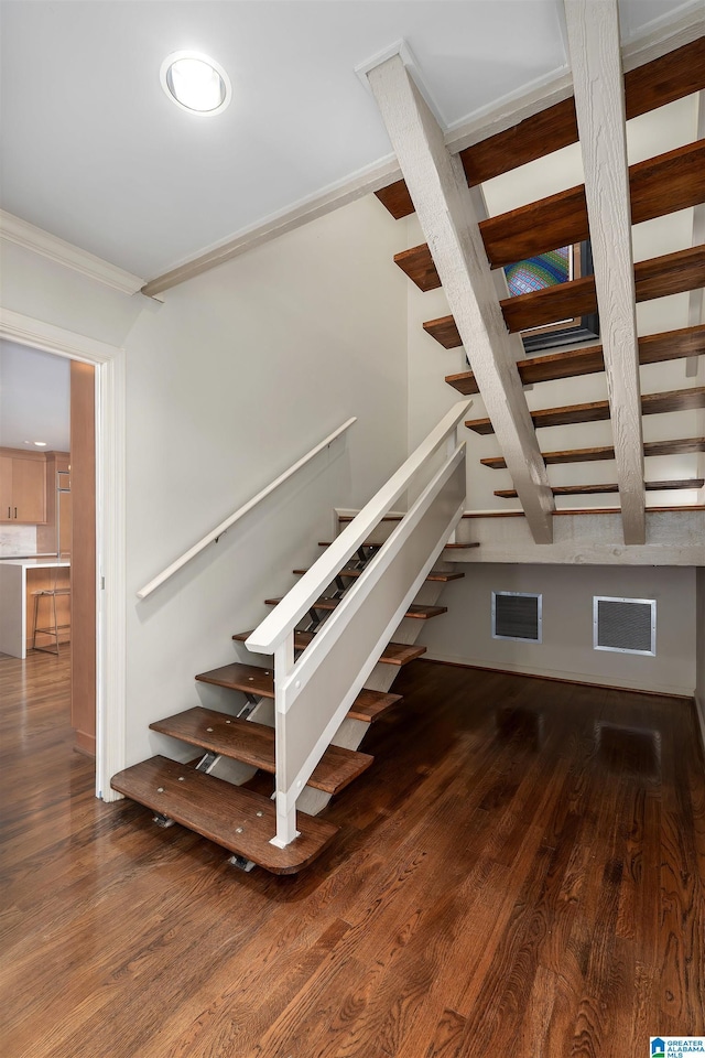 staircase with ornamental molding, wood finished floors, and visible vents