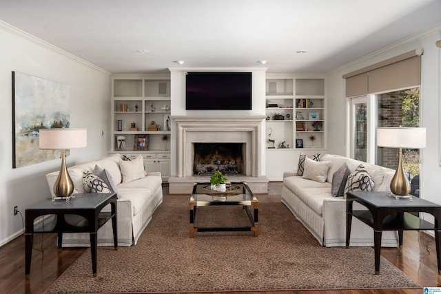 living room with baseboards, a fireplace with raised hearth, wood finished floors, crown molding, and built in shelves