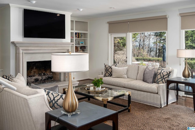 living area with built in shelves, crown molding, a fireplace, and wood finished floors