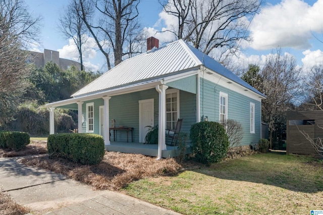 view of side of home featuring metal roof, a porch, a chimney, and a lawn