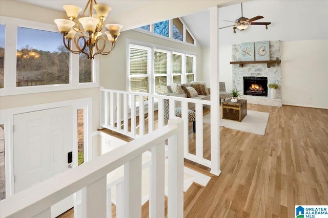 interior space featuring light wood-type flooring, ceiling fan with notable chandelier, high vaulted ceiling, and a stone fireplace