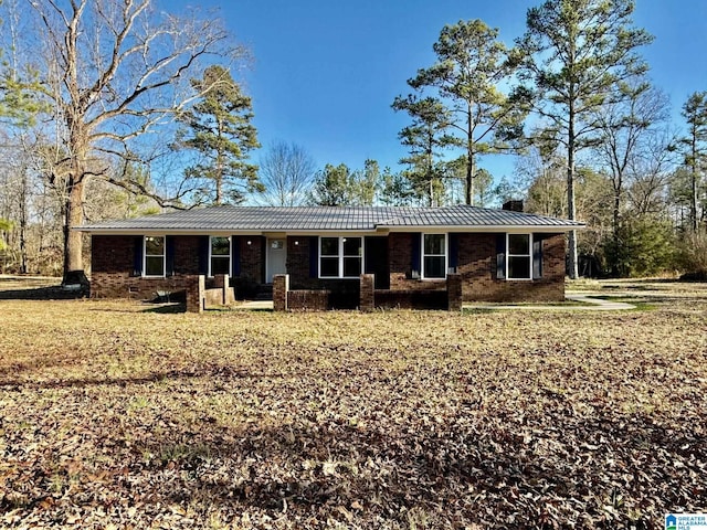 ranch-style home featuring a standing seam roof, brick siding, metal roof, and a chimney