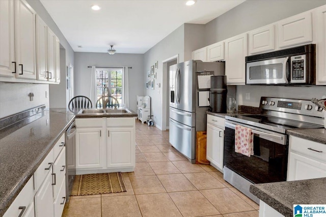 kitchen with light tile patterned floors, stainless steel appliances, a peninsula, white cabinets, and dark countertops